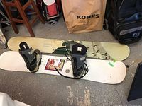 Two Sequence snowboards, one with bindings and a pair of boots attached, resting on garage floor with tools and bags visible.