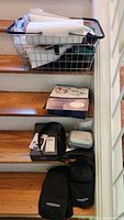 Photo showing large wire basket and items including Slendertone belt pouches, a plastic case, and a box on wooden steps.