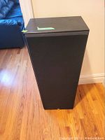 Full view of front of one black JBL speaker upright on hardwood floor.