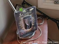 Front view of Cobra radar detector in original sealed packaging on a wooden table with window in background.