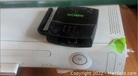 Xbox 360 console front with power button and disc tray visible showing some wear and green tape residue.