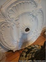 Close-up photo showing the white large ceiling medallion with ornate floral and leaf detailing and a center hole for fixture attachment.