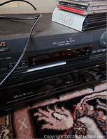 Front and top view of the black JVC VHS player with power button, branding, and input ports visible.