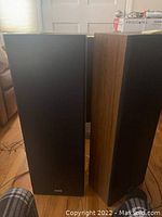 Two tall brown Sanyo speakers with black front grilles standing upright on a wooden floor in a room.