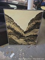 Framed wall art placed on a concrete floor with visible garage background. Shows entire artwork and frame condition.