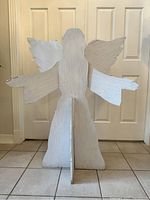 Backside of a large white wooden angel figure showing two separate wing parts connected and central base for standing.