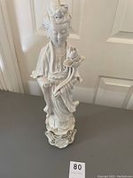 Front view of the 18-inch white ceramic statue showing detailed facial features, headpiece, beaded necklace, and the lotus flower held in the left hand.