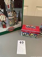 Photo showing the boxed phone booth and skating pond porcelain village decorations with a note indicating item sizes and descriptions.