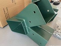 Close-up photo of a green painted heavy metal jungle gym bracket showing mounting holes and welded construction.