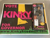 Image showing poster with 'VOTE KINKY FRIEDMAN FOR GOVERNOR' text and action figure in box on top of it.