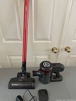Full view of vacuum components: handheld vacuum unit, red extension wand, motorized brush head, charger on table