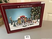 Box of the St. Nicholas Square Village Collection skating pond holiday scene showing the full winter skating pond setup with figures and trees.