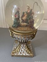 Front view of the snow globe showing the nativity scene figurine inside, with the ornate decorative base visible.