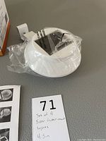 Photo of one white solar gutter mount light in plastic packaging with mounting bracket and a piece of paper with handwritten lot number and details.