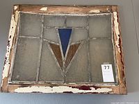 Front view of the vintage stained glass panel showing geometric shapes in blue and brown within textured clear glass, framed in aged wood with chipped paint.
