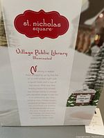Box front showing St. Nicholas Square branding and product description for Village Public Library illuminated decoration.
