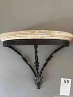 Front view of a wall mounted stand showing a light stone top and black twisted metal supports with decorative elements
