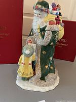 Full side view of Waterford cookie jar showing Santa dressed in green robe with gold stars, carrying gifts with child in yellow coat beside him.
