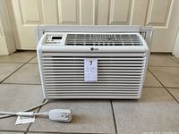 Front view of LG window unit air conditioner showing grille, electronic control panel, power cord with plug.