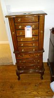 Front view of wooden jewelry box with multiple drawers and brass knobs, standing on carved legs.