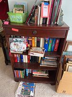 Books on wooden shelving unit featuring assorted books including cookbooks and fiction on four shelves, also decorative bookends on top shelf.