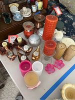 Full view of assortment of candles and candle holders displayed on white table including pillar candles, votive candles, scented candle, bird-shaped holders and berry decorated holders.