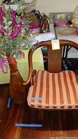 Front view of wooden armchair with striped cushion and vase with artificial plant in background