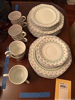 Photo showing stack of octagonal and round plates with small floral pattern in red and blue with green vines on white china with several cups.