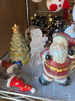 Photo showing ceramic Santa Claus, Christmas tree candle holder, frosted snowman candle holder, and small figurines.