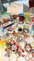 Photo showing a large variety of colorful clip-on earrings and bracelets with a sign noting 'Clip-on Earrings, Screw on Earrings, Bracelets'.