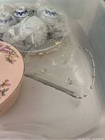Photo showing white ceramic teacups with blue patterns wrapped in bubble wrap, clear glass platter with scalloped edges, and pink floral round box.
