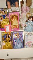Photo showing boxed Snow White, Belle, and Cinderella Barbie dolls along with one vintage doll in a blue floral dress standing on a shelf.