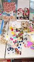 Wide view of earrings and pins spread over a table and partially in boxes, including various colors and styles of pierced earrings and pins.