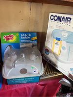 Photo showing Conair Foot Spa box, American Classic washerless faucet box, and Scotch-Brite Tub & Tile Scrubber packaging together on display.