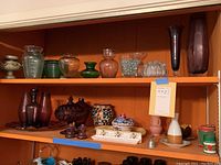 Two shelves displaying a variety of glass vases, ceramic bowls, and decorative objects including small jars, candlesticks, and a ceramic covered container.