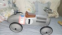 Side angle of silver kids push car on fabric background showing brown seat, wheels, and number 1 decal