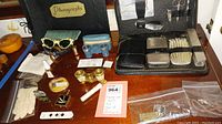 Overall view of the lot showing the photograph album, sunglasses, opera glasses, and grooming kit laid out on a wooden surface.