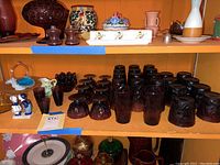 Shelf with multiple purple glass sherbet cups and tumblers along with polychrome pottery and glass items