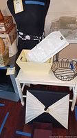 Close-up of white stool holding a pale yellow rectangular box, a black wire basket, and other storage boxes visible around.