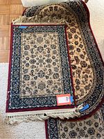 Three stacked hallway rugs showing the smallest rectangular rug on top with beige, blue, and red floral pattern and fringes, and two larger oval rugs underneath with beige and dark blue floral designs.