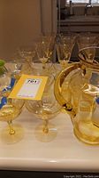 Yellow glass pitcher and various yellow tinted stemmed glasses with visible chip in one glass.