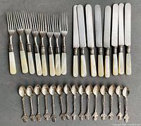 Top-down view of the full set showing 8 forks and 8 knives with mother of pearl handles grouped together above 15 commemorative spoons with decorative twisted handles.