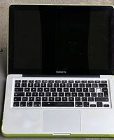 Front view of Apple MacBook Pro laptop open, showing keyboard and screen with green protective cover on sides.