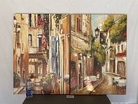 Full view of two cityscape canvas prints side by side, showing architectural details, flowers, and outdoor seating.