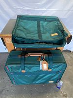 Two green Fliteline California luggage pieces, one placed on a table and the other leaning against it, showing external zip pockets and brown handles.