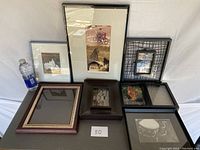 Group of seven frames displayed on a table with various artwork and photographs inside. Bottle of water included for scale.