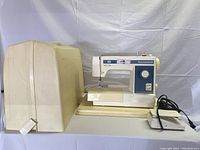 Side view of Kenmore sewing machine with hard protective cover in cream color.