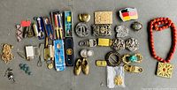 Lot overview showing belt buckles, pens, jewelry, and decorative items spread out on a surface