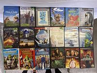 Photo showing 20 DVD cases stacked in four rows, includes titles like Shrek series, Night at the Museum, Transformers, and others.