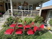 Seven red chairs placed on grass outside a porch, showing the overall set and setting.
